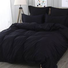 a bed with black comforter and pillows in a room next to a lamp on a wooden floor