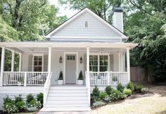 a white house with porches and steps leading up to the front door is surrounded by greenery