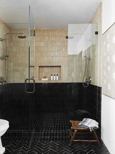 a black and white tiled bathroom with a wooden stool next to the shower stall,