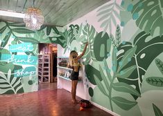 a woman standing in front of a wall with green leaves on it and writing on the wall