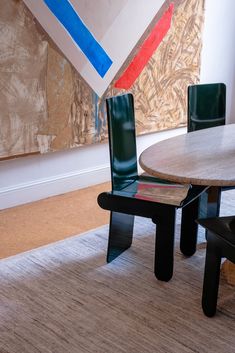 two chairs and a table in front of a wall with paintings on the walls behind them