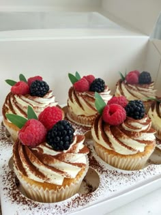 cupcakes with white frosting and raspberries on top are displayed in a box