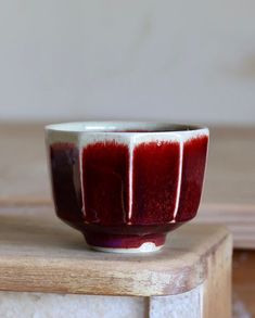 a small red and white bowl sitting on top of a wooden table next to a wall