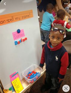 a young boy standing in front of a white board with magnets on it's side