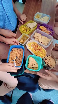 several children sitting at a table with containers of food in front of them and one child holding a fork