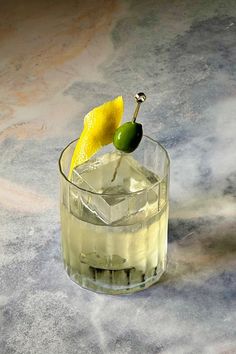 a glass filled with ice and a lemon on the rim next to a green olive