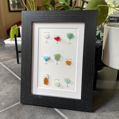 a framed picture with different colored glasses on it next to a potted green plant