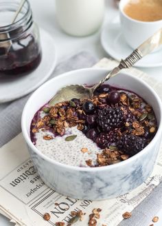 a bowl of oatmeal with berries and granola in it next to a cup of coffee