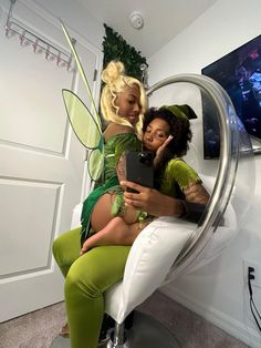 two women dressed as tinkerbells sitting on a chair with a cell phone