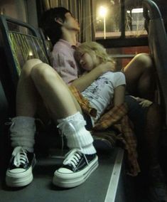 two people sitting on a bus next to each other with their feet propped up against the seat