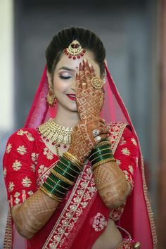 a woman in a red and gold bridal outfit holding her hands up to her face