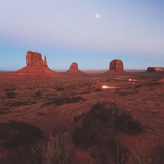 the desert is full of red rocks and green bushes, with a moon in the sky