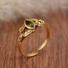 a gold ring with an oval green stone and leaves on the side, sitting on a wooden surface