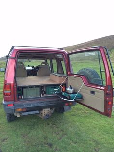 the back end of a red truck with its cargo compartment open in a grassy field