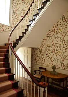 a stair case next to a table with a vase on it and wall paper behind it