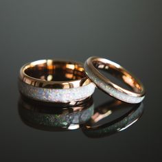 two gold wedding bands with white opal inlays on a black table top