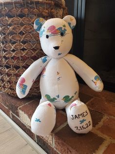 a white teddy bear sitting next to a basket on the fireplace mantel with name written on it