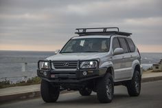 a white suv driving down the road next to the ocean