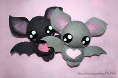 two little bats with big eyes are sitting on a pink surface and one is holding a heart