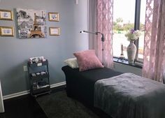 a bed sitting in front of a window next to a black table with pink pillows