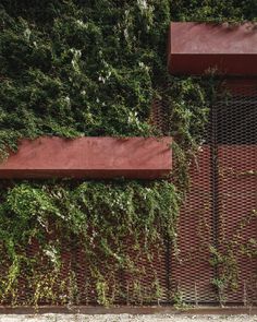 a red bench sitting next to a tall brick wall covered in green plants and vines