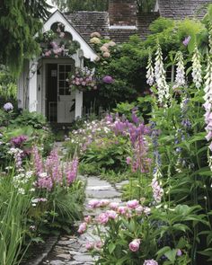 a garden with lots of purple flowers and greenery in front of a white house