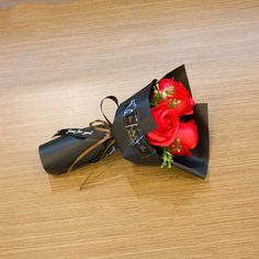 a bouquet of red roses in a black paper hat on a wooden table with ribbon