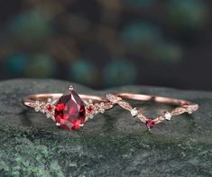 two wedding rings with red stones and diamonds on top of a green stone slab in front of a blurry background