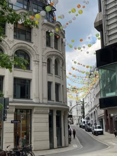 many balloons are floating in the air above a street lined with buildings and people walking on the sidewalk