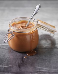 a glass jar filled with caramel sauce and two silver spoons