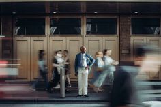 a man standing in front of a building next to a crosswalk with people walking by