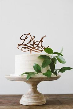 a white cake topped with a wooden mr and mrs topper next to green leaves