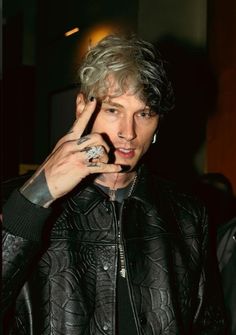 a man with grey hair wearing a black leather jacket and holding his hand up to his face