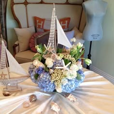 a table topped with a vase filled with blue flowers next to a sailboat on top of a bed