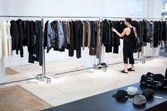 a woman standing in front of a rack of clothes and looking at the shirts on display