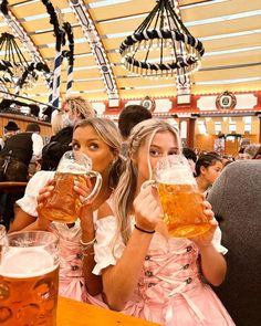 two beautiful women sitting at a table with mugs of beer