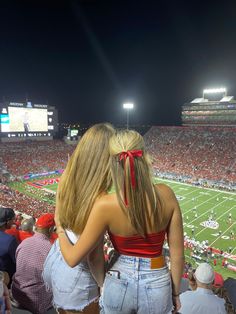 two women standing on the sidelines at a football game, with their backs to each other