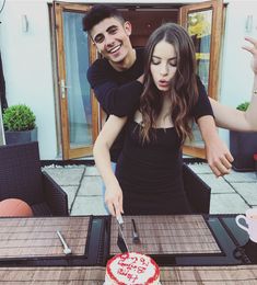 a young man and woman cutting into a heart - shaped cake on top of a table