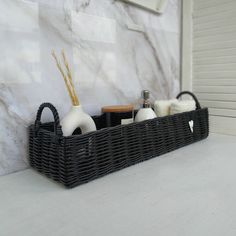 a black basket with soap and lotion in it sitting on a counter next to a marble wall