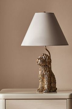 a golden dog lamp sitting on top of a white dresser next to a beige wall