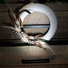 a wreath with feathers on it sitting on a dresser doorknobs in front of a white ring