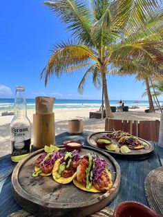 some tacos and drinks on a table at the beach with palm trees in the background