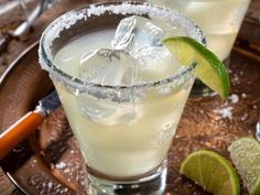 two glasses filled with ice and limes on top of a plate next to silverware