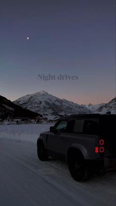 the truck is driving down the road in the snow at night with mountains in the background