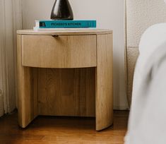 a nightstand with a book on top of it next to a white wall and wooden floor