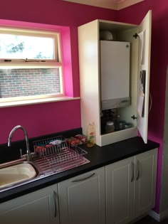 a kitchen with pink walls and white cupboards in the corner next to a sink