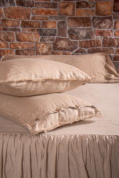 two pillows on top of a bed in front of a brick wall and headboard