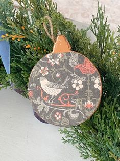 a christmas ornament hanging from a tree branch with flowers and birds on it