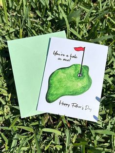 two greeting cards featuring a green golf club and a red flag on top of some grass