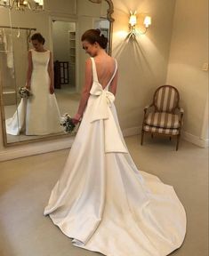 a woman standing in front of a mirror wearing a white dress with a bow on the back